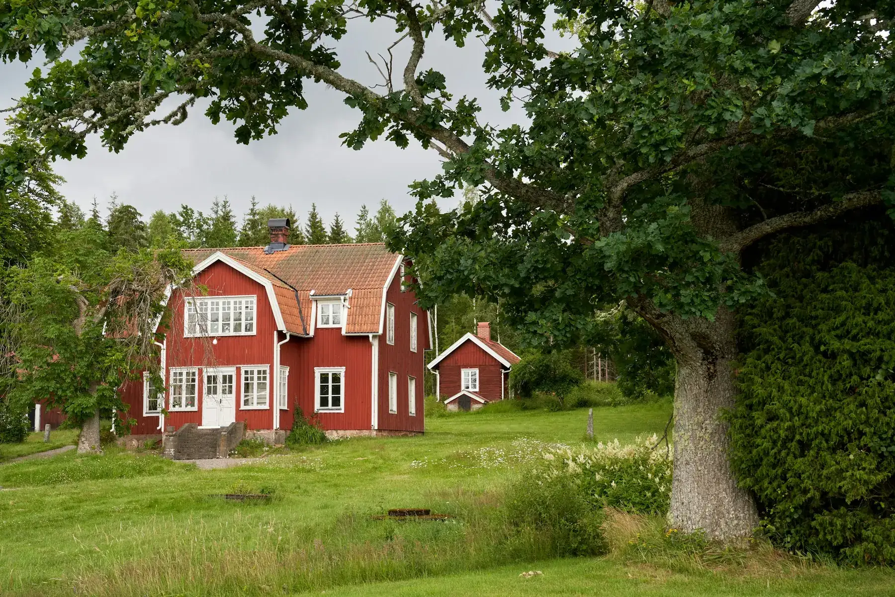 Ett falurött trähus med vita knutar på en grön äng.